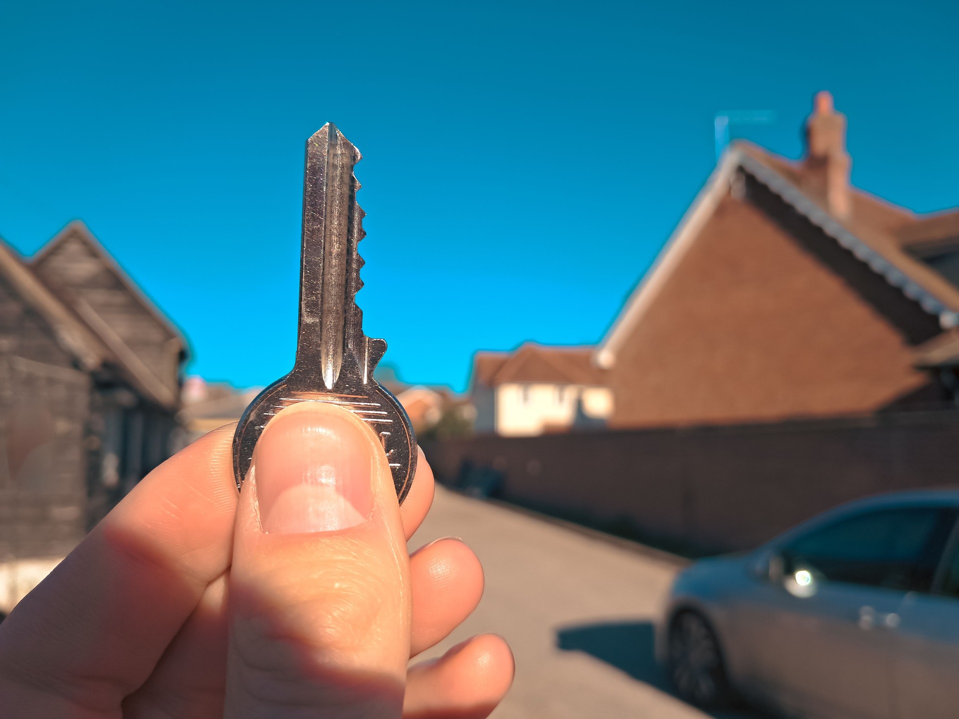 A new home purchase concept with a key in hand and a house in the background.